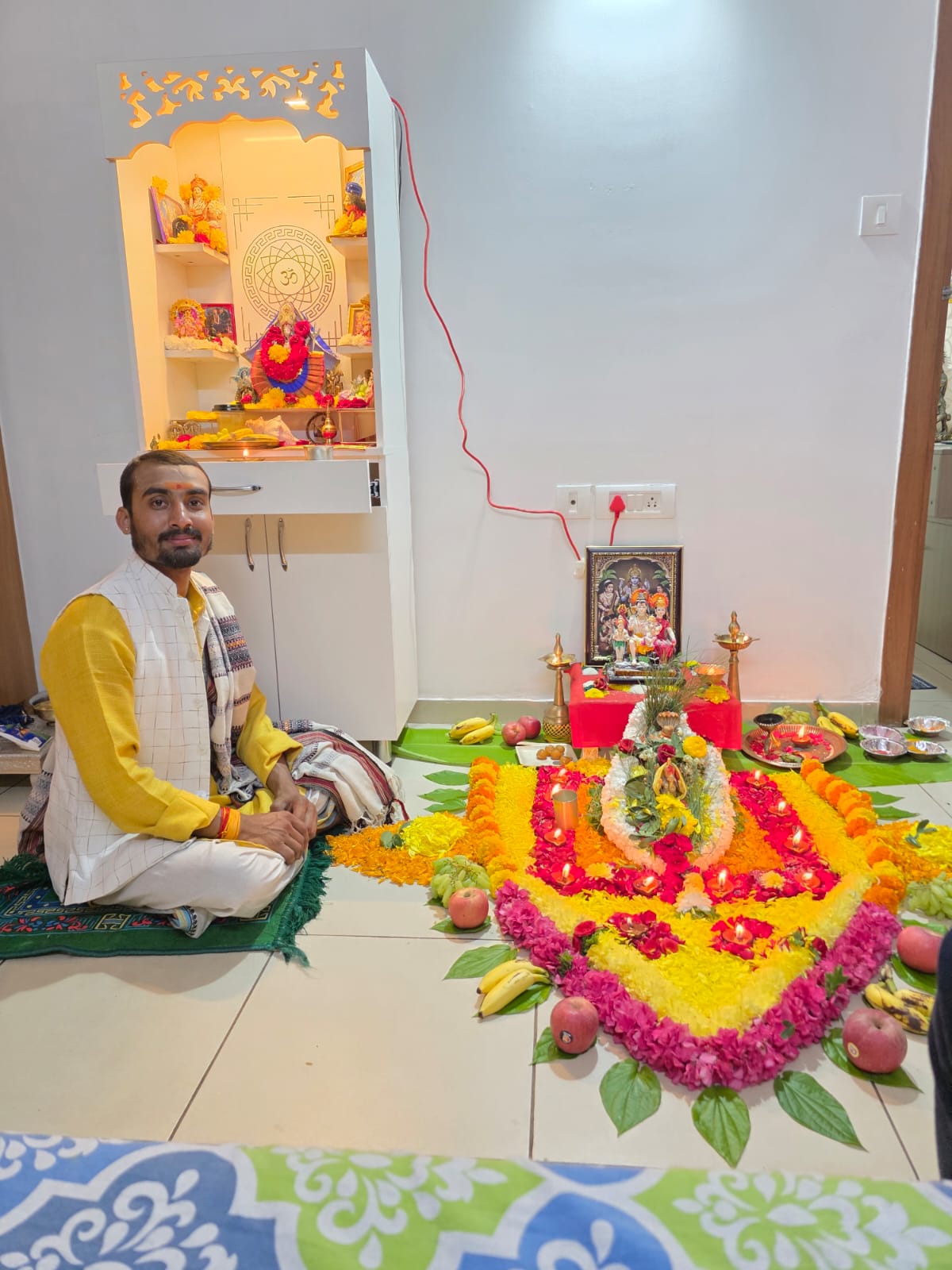 Pandit seated at home altar with floral rangoli